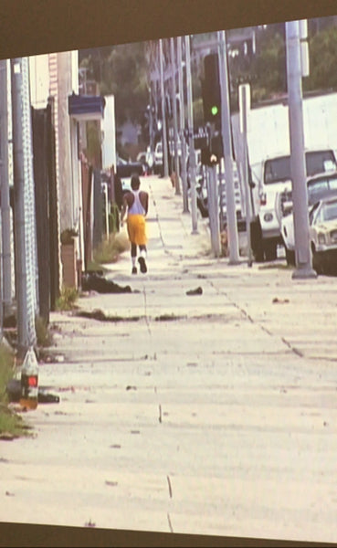 a still from one of mark bradford’s pieces with a person walking on the streets. 