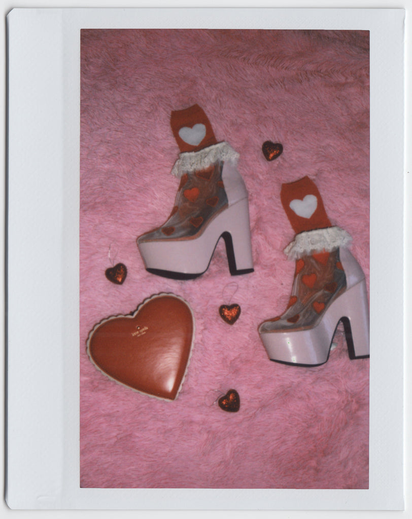 still life of heart shaped kate spade clutch, heart shaped ornaments and heart print heels and heart print socks.
