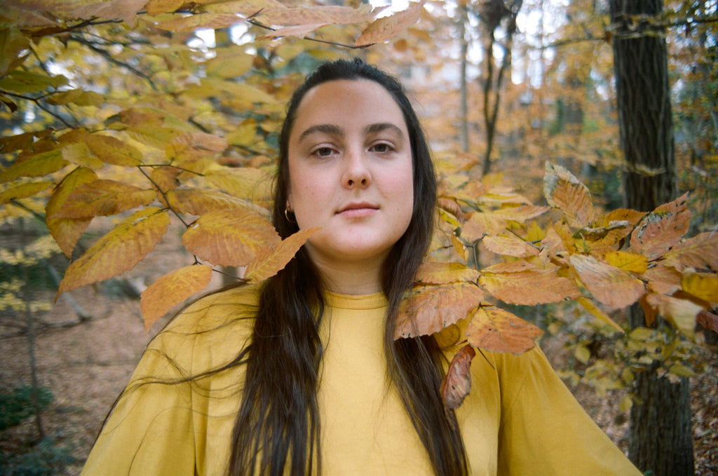 delcey in a yellow shirt standing in the woods.