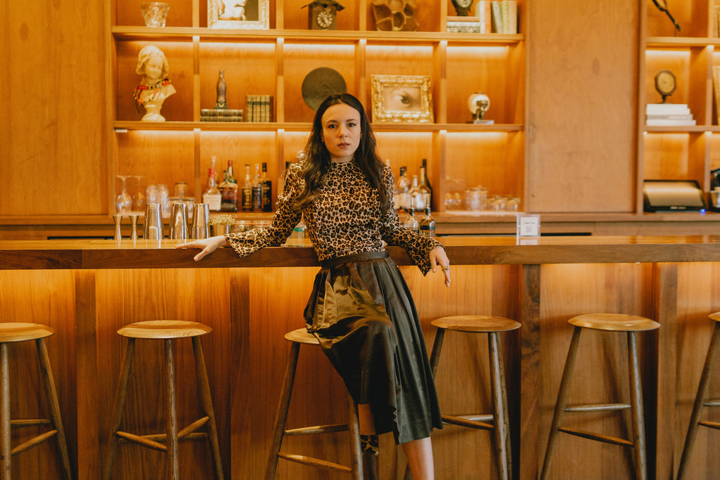 sarah amorelli in leopard print top, brown skirt and leopard print heels sitting at a bar.