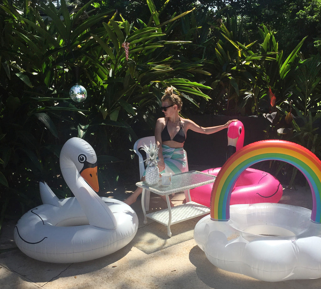 person posing near flamingo and rainbow floats. 
