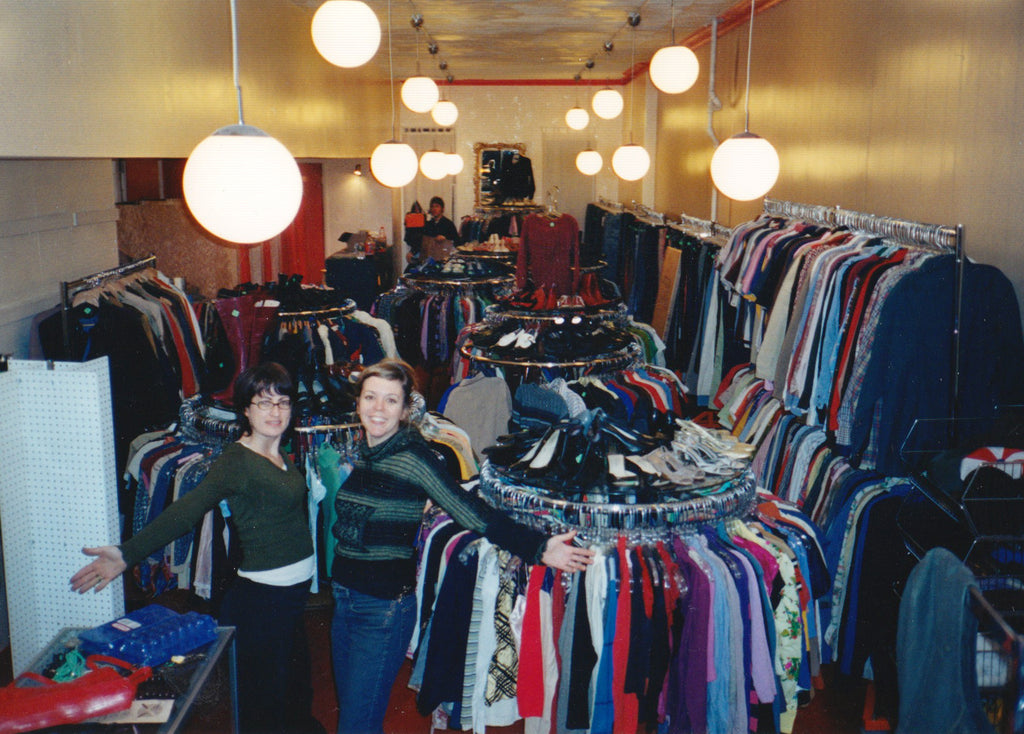 co-owners of park slope's first location. two women standing with arms out among round racks of clothing
