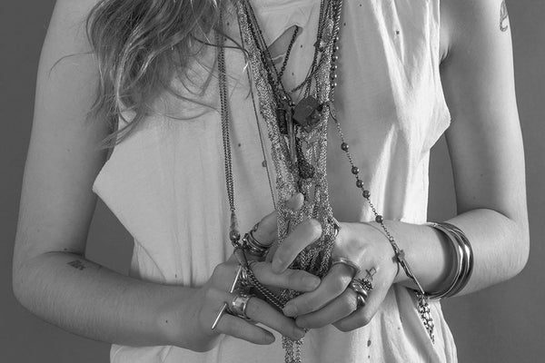 detail of model in stacked silver necklaces, rings and ripped white tank top.