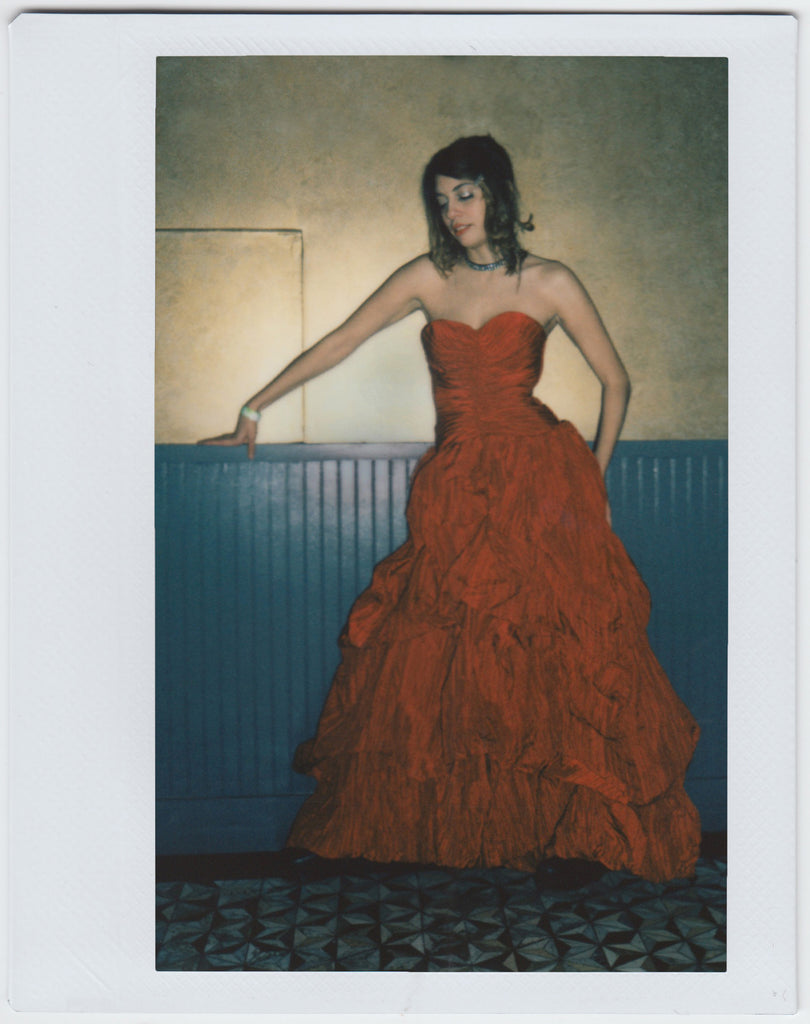 person posing in full body shot, looking down, wearing a long red dress - polaroid style. 