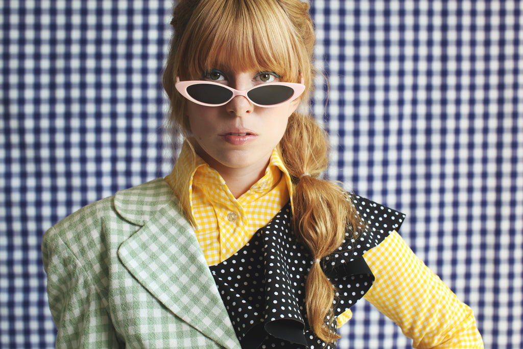 model in slim sunglasses mixed check prints and polka dots in front of a checkerd backdrop .