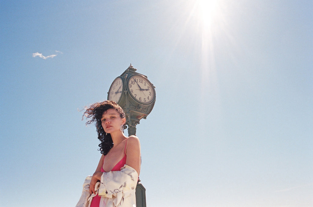 model in swimwear and robe in front of clock on boardwalk.