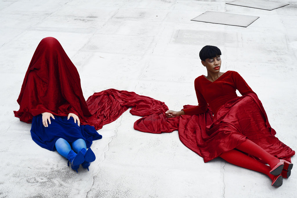 two models sitting on a roof in velvet dresses with a velvet blanket draped over them.