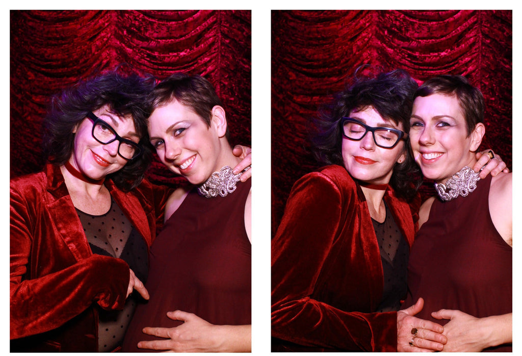 first image: duo smiling, one gesturing to pregnant belly, and red velvet backdrop; second image: duo posing and hugging, hands on belly.