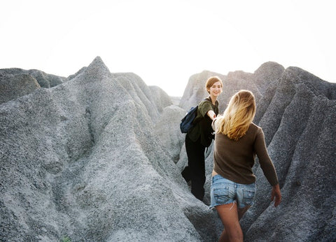 Brunette woman reaching out hand to help other blond woman to climb a mountain