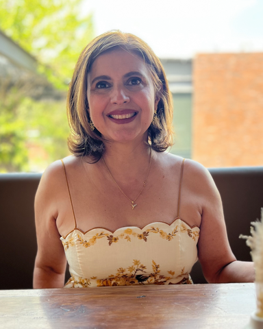 Portrait of author/designer Claudia Quintanilla, seated on a chair, with shoulder length hair and wearing a yellow sundress