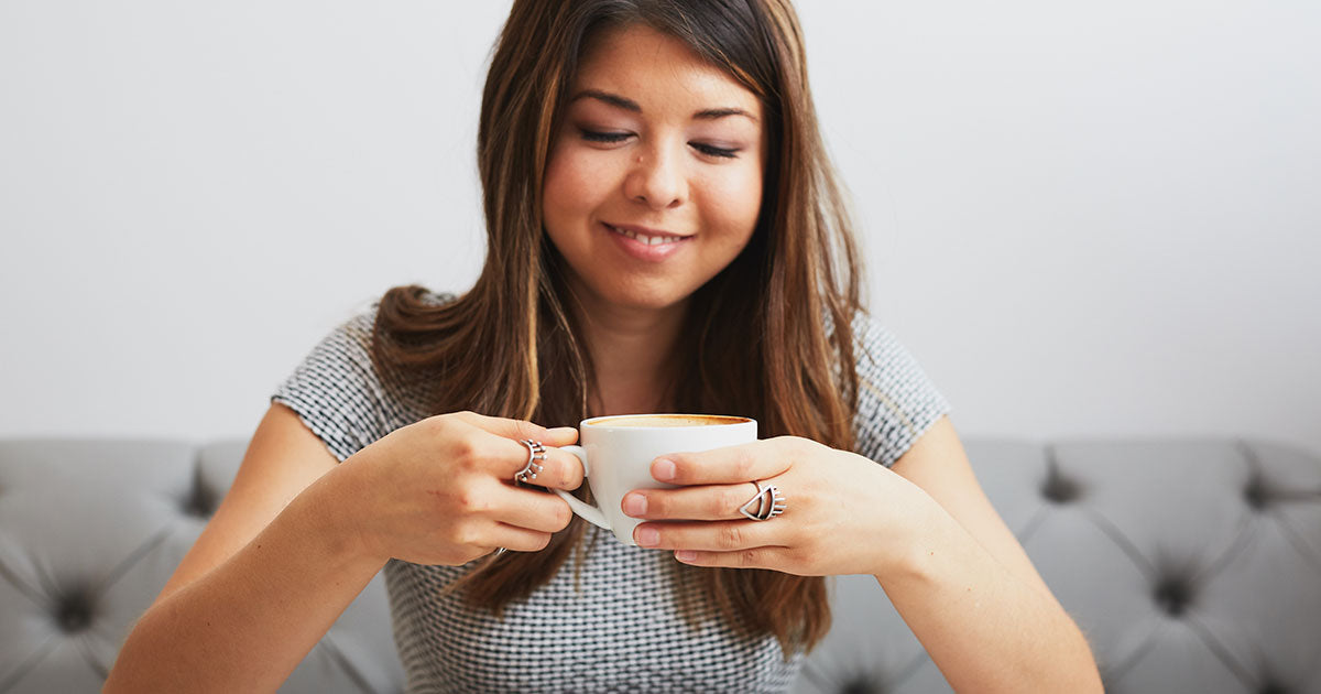 a woman smiling while holding and looking at a cup of coffee