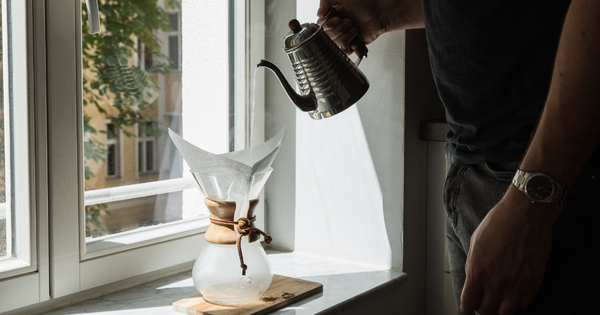 A person preparing their pour-over device by saturating the coffee filter with hot water.