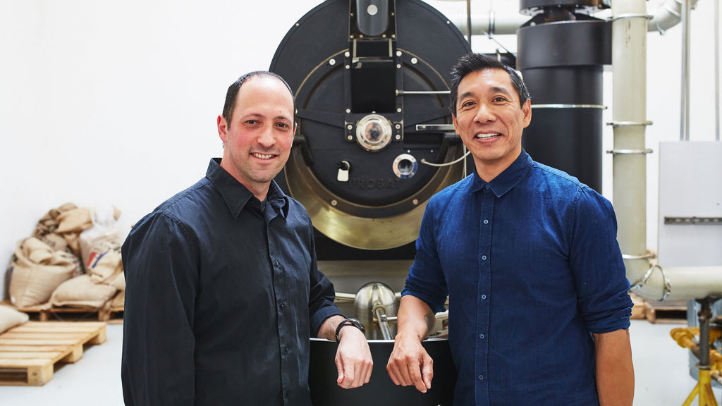 caffe luxxe owners smiling in front of a coffee roaster