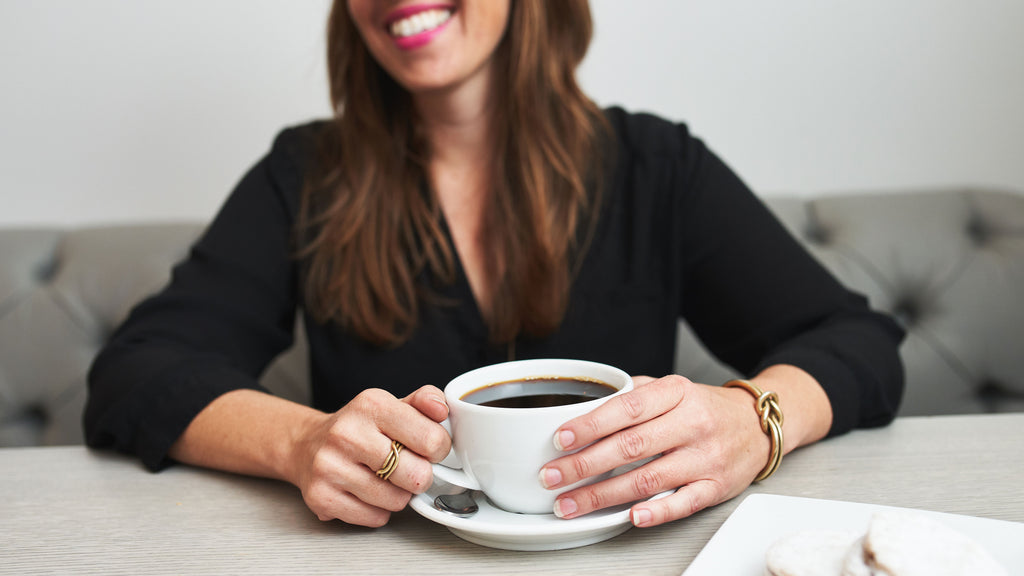 a woman smiling while holding a cup of coffee