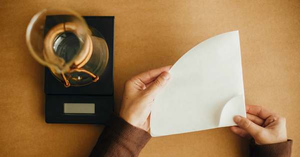 A person holding a paper coffee filter with a pour over coffee maker in front of them.