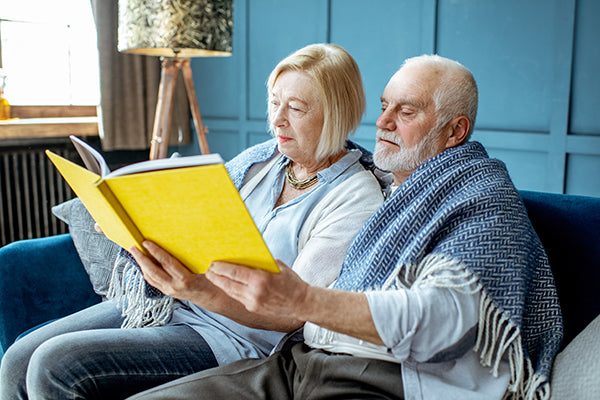 Older couple sitting on sofa looking at photo album.