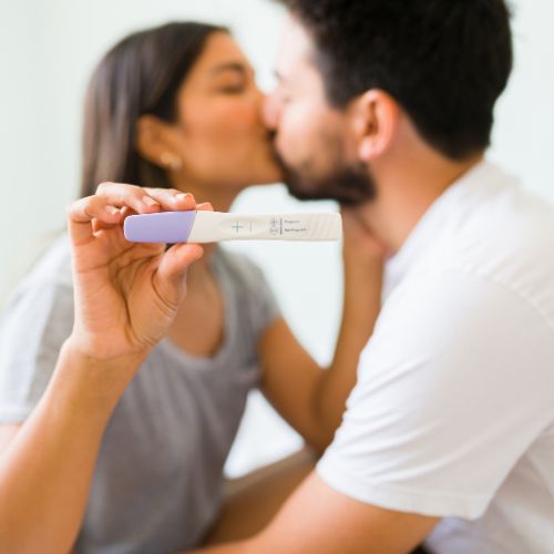 young couple kissing and holding up positive pregnancy test