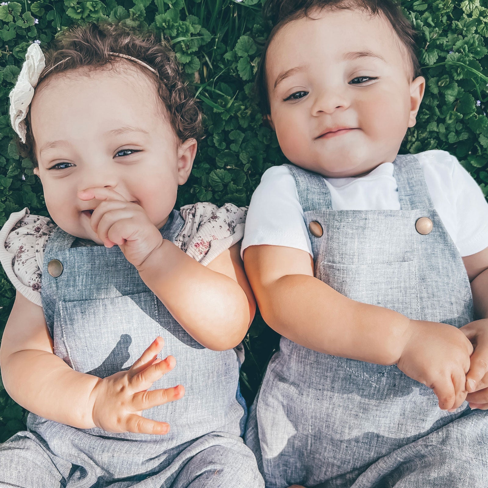 baby boy and girl twins in matching blue overalls lying in the grass