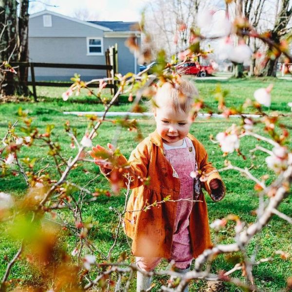 toddler girl wearing linen baby romper playing in cherry blossoms