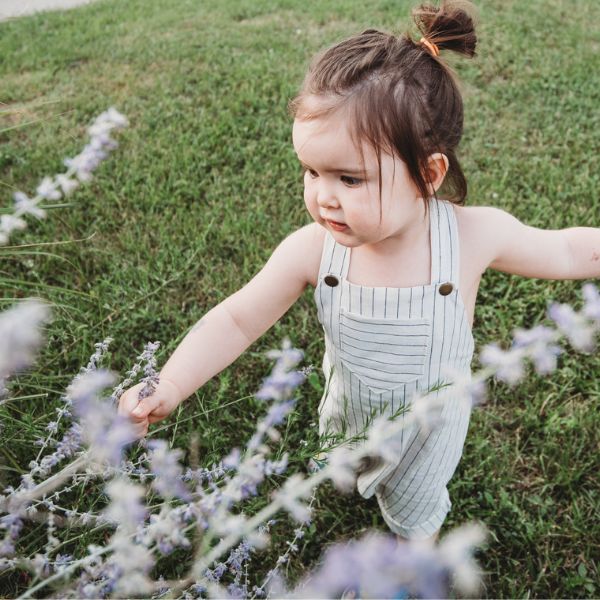 toddler girl wearing white stripe linen romper playing in lavender blooms