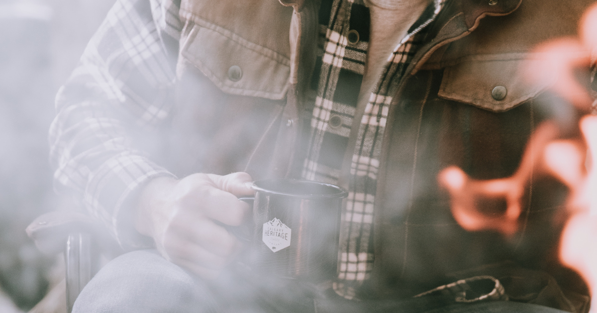 Guy sitting around fire drinking coffee