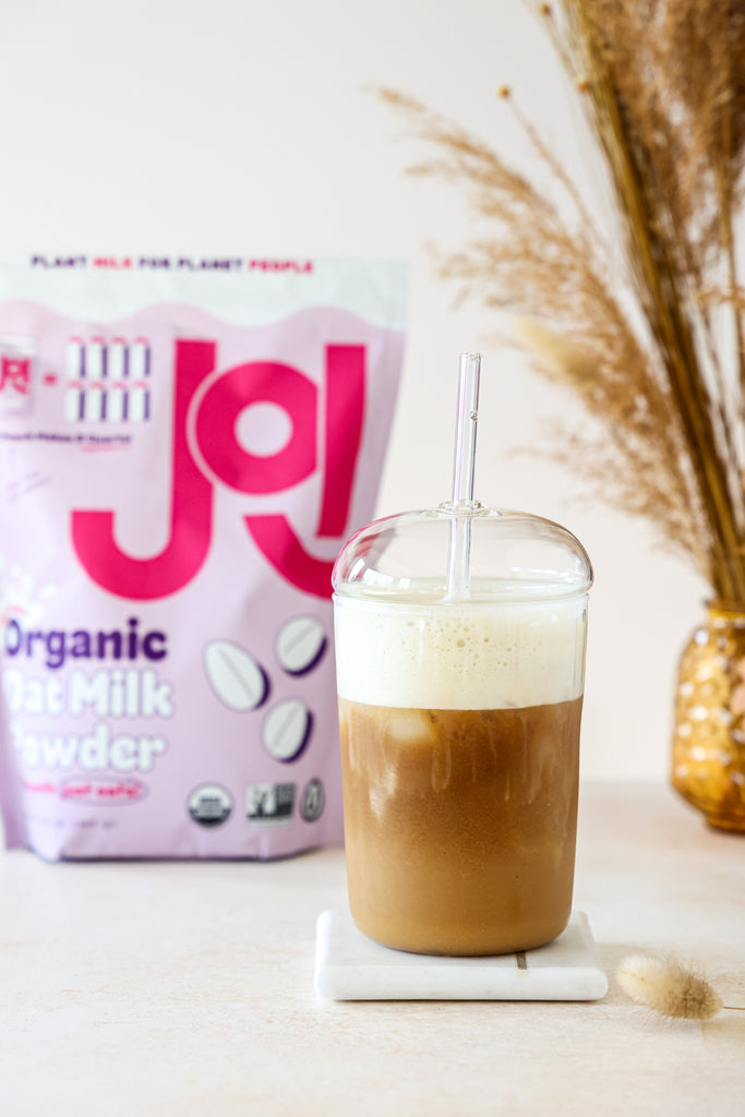 glass of iced oat milk latte in front of JOI oat milk powder pouch