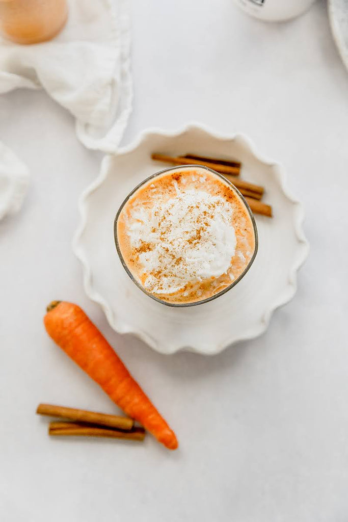 top view of carrot cake smoothie in a glass next to a carrot and cinnamon stick