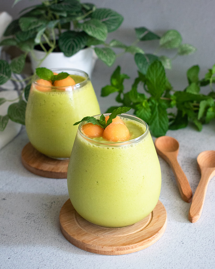2 glasses of green melon smoothie topped with canteloupe balls and mint in background