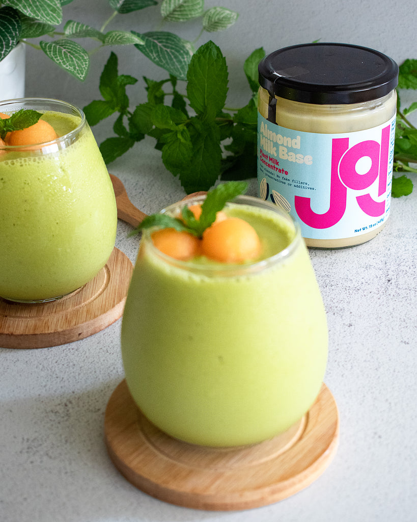 2 glasses of green melon smoothie topped with canteloupe balls and JOI jar in rear
