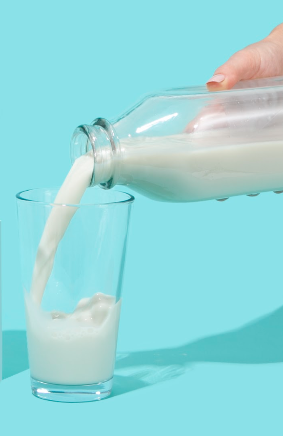 hand holding glass jar of milk being poured into glass