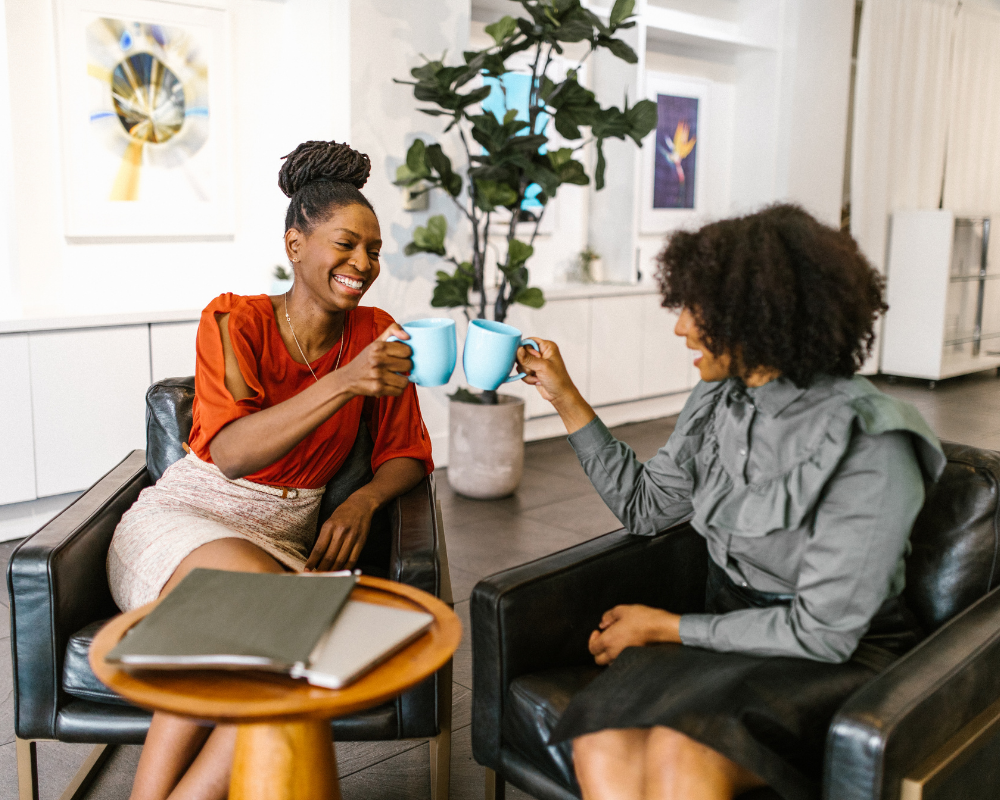 two women "cheers" with coffee mugs