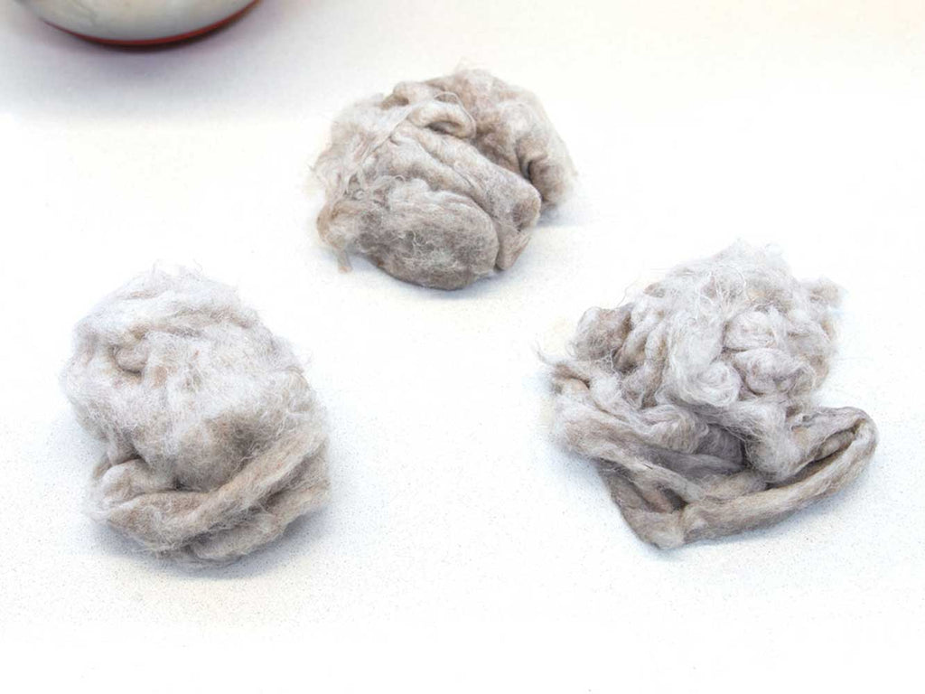 Three fist sized piles of wet carded wool on a white countertop.