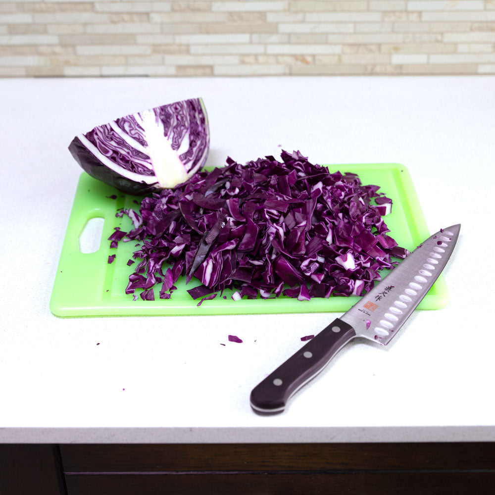 Half a head of chopped red cabbage on a cutting board. A knife is laying on right side of the board.