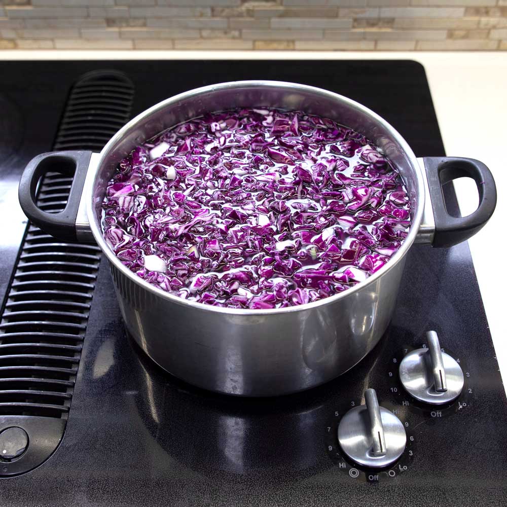 A stainless steel pot filled with chopped red cabbage and water sitting on a stovetop.