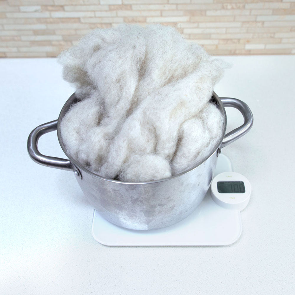 A stainless steel pot filled sitting on a kitchen scale with fluffy carded wool inside the pot