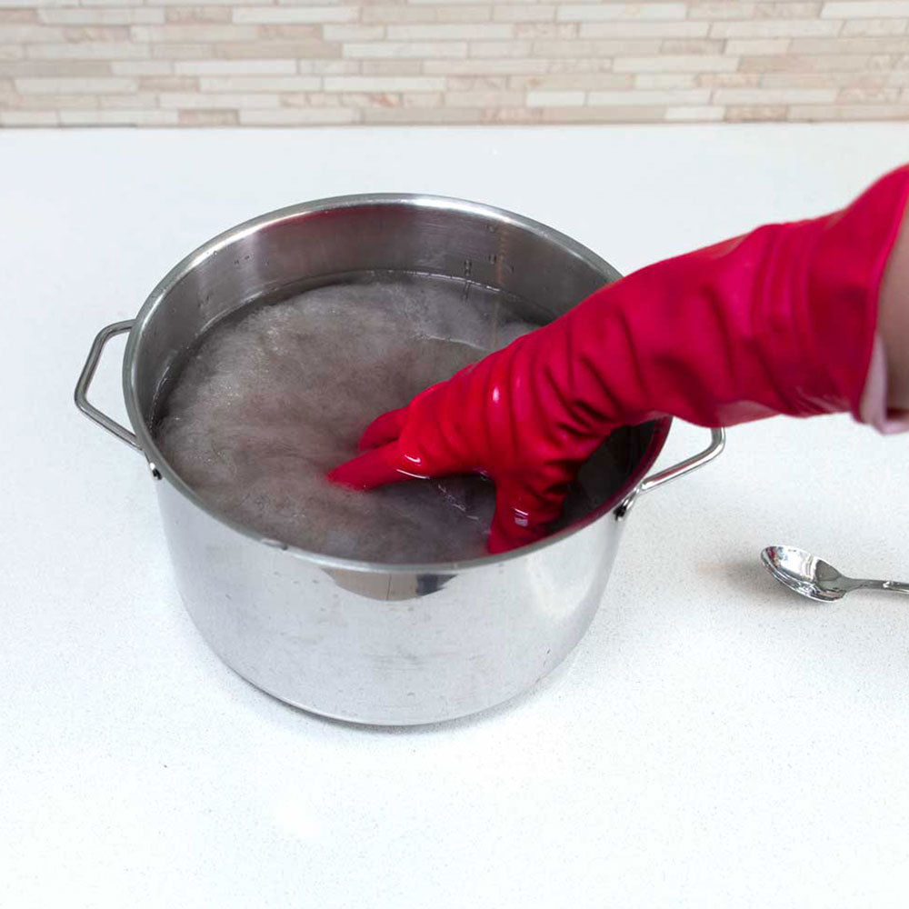 Submerging carded wool into a stainless steel pot filled with a warm water Alum solution.