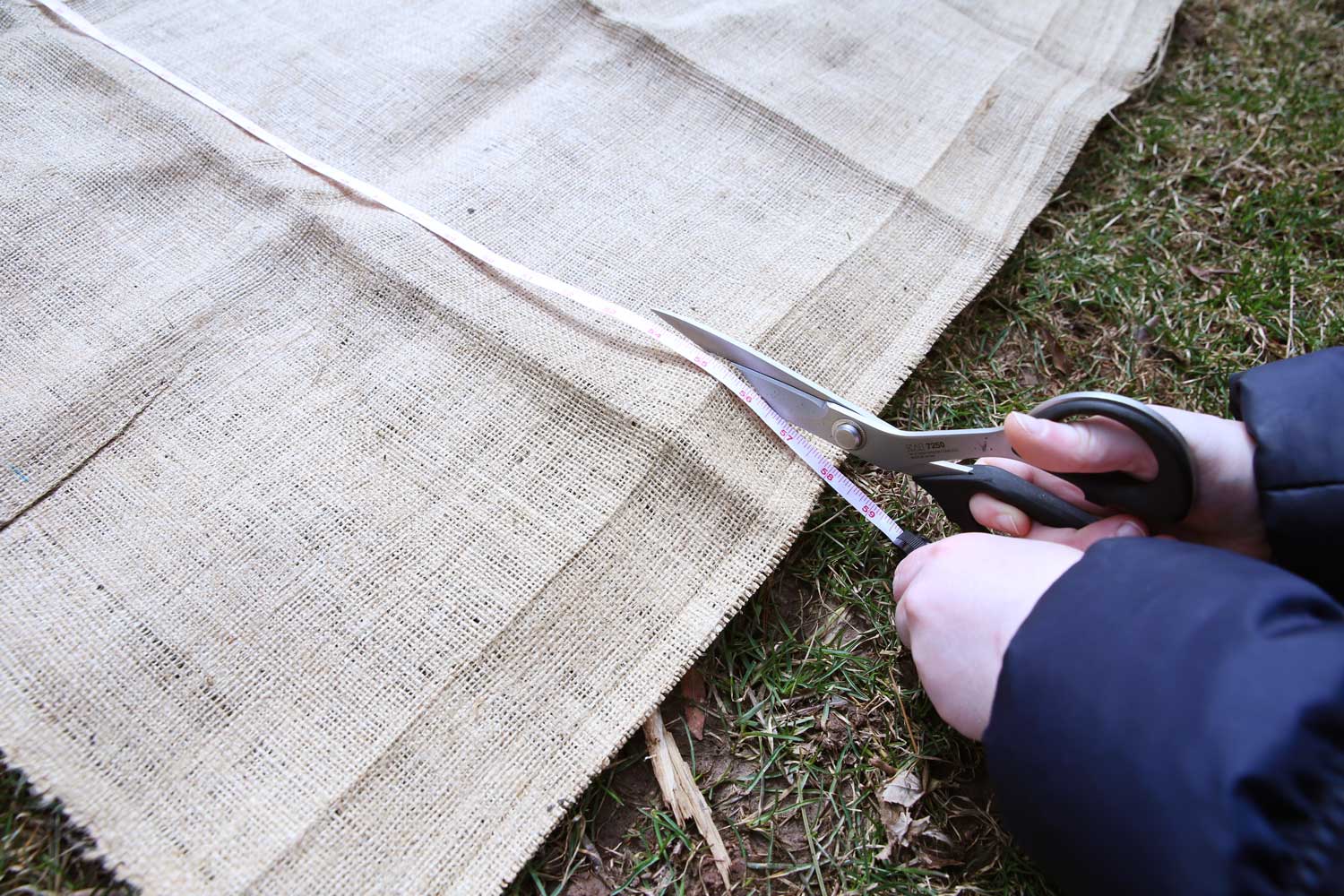Hands using scissors to cut into burlap, using a soft tape measure as a cutting guide