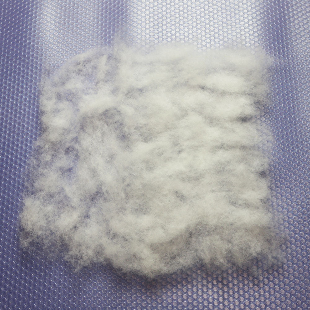 A square of white carded wool. The left side is one layer of wool fluff thick. The right side has two layers of wool fluff.