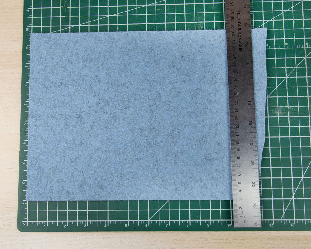 A rectangle of blue felt on a green cutting mat. A silver ruler is on top of the blue felt.