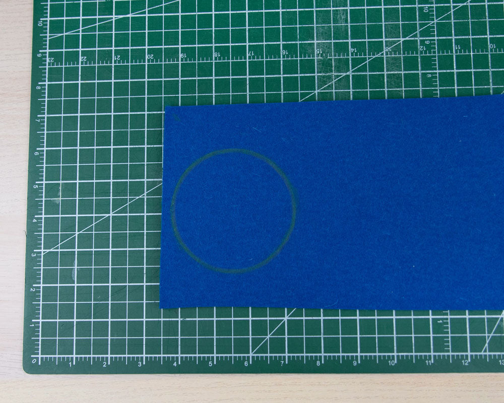 A rectangle of dark blue felt on a green cutting mat. There is a circle in yellow drawn onto the dark blue felt.