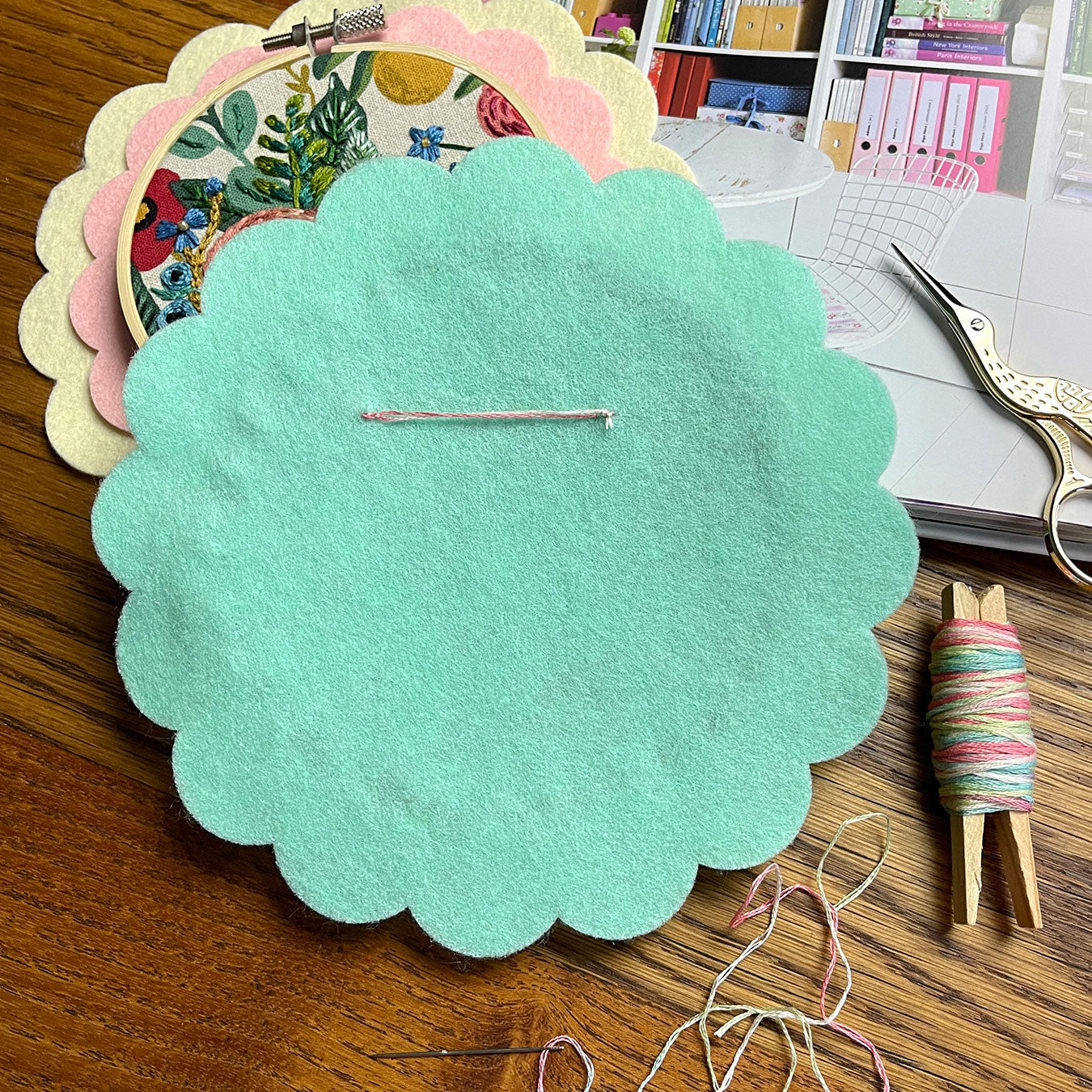 The back of an embroidery hoop with a scalloped felt circle as the backing. There is a line of handsewn embroidery thread near the top of the hoop backing to act as a hook.