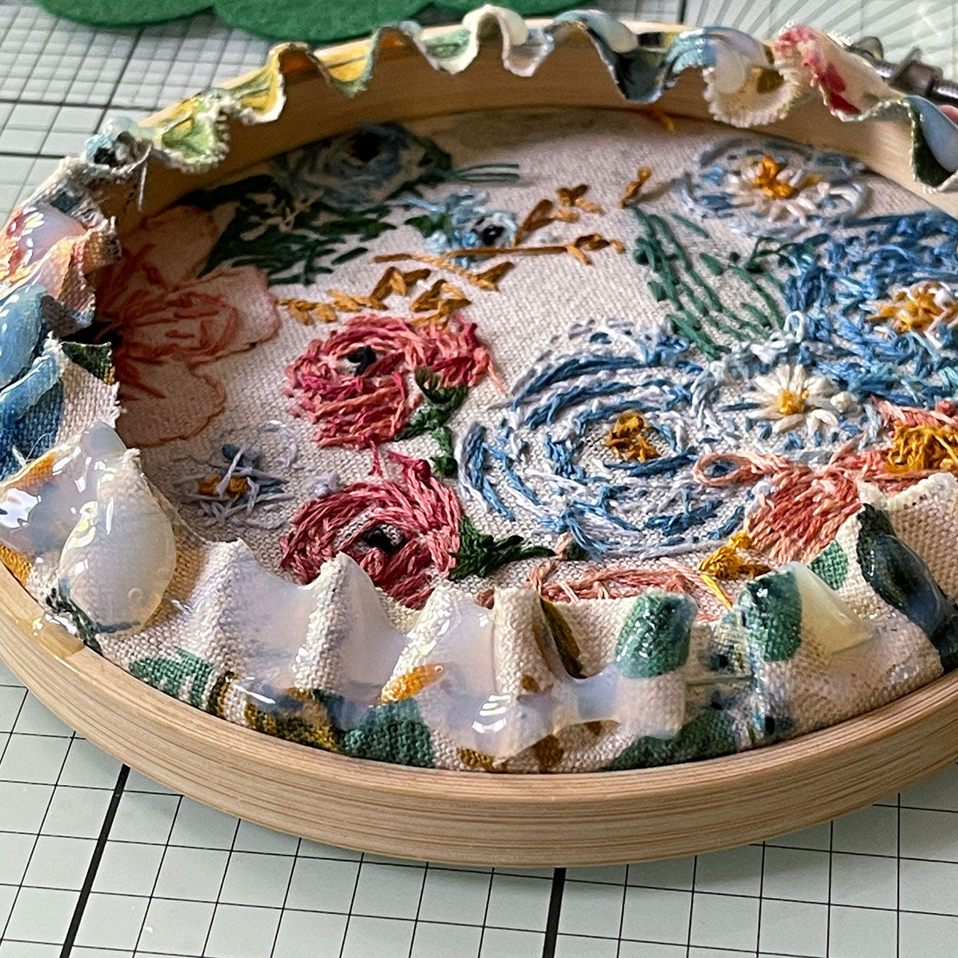 An embroidery hoop with fabric is laying face down on a cutting mat. The back edges are gathered and there is glue on the fabric.