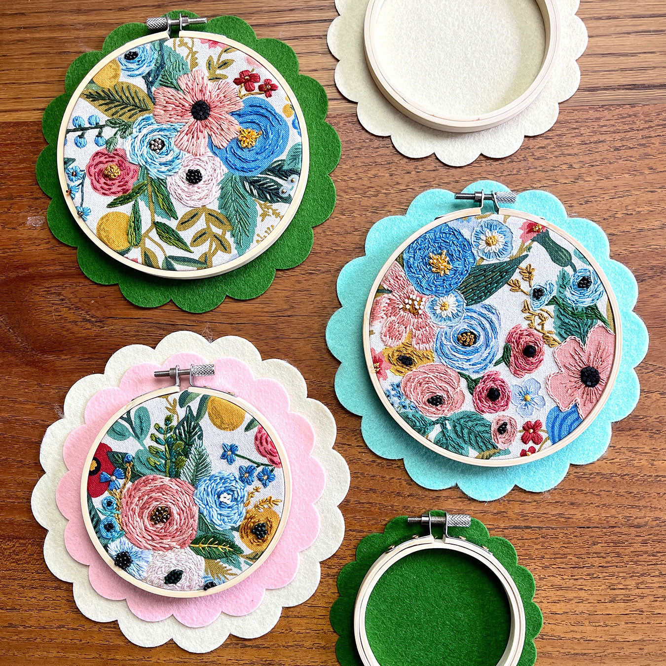 Five embroidery hoops a varying sizes are laid on top of a wooden table. Each hoop has a scalloped felt circle as it's backing.