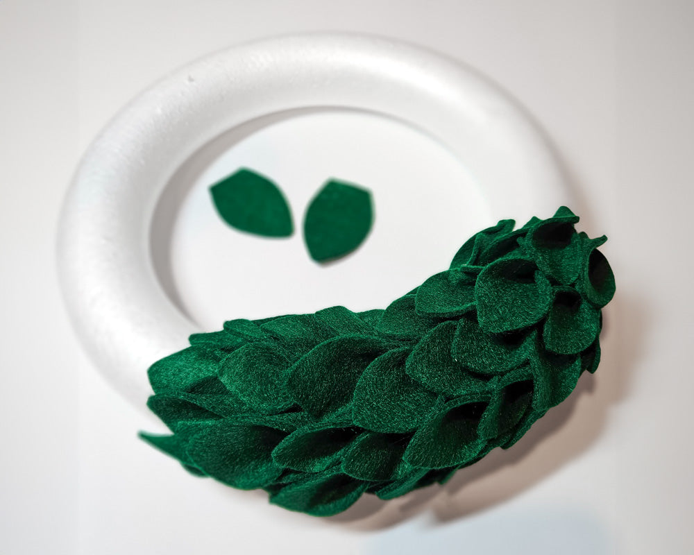 Adding green felt leaves for the holiday wreath with a styrofoam ring form