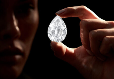 A Man looking at very large pear shaped diamond, holding between his thumb and fore finger