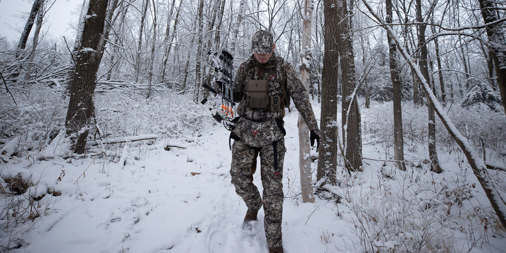 male bow hunter walking through forest on winter hunt