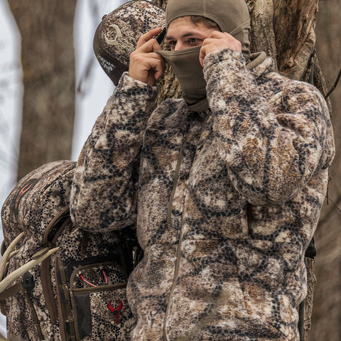 hunter in tree stand pulling gaiter over face