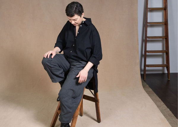 Eva Cassis is perched on a stool and looking down at the ground. She is wearing dark-coloured, ethically produced clothing.