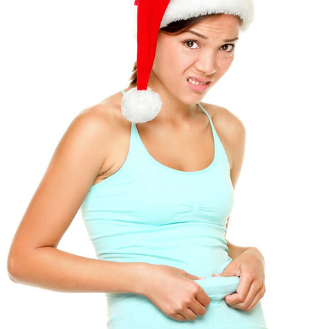 Fit young woman in Santa hat pinching belly after holidays