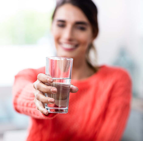 Smiling young woman offering a glass of water